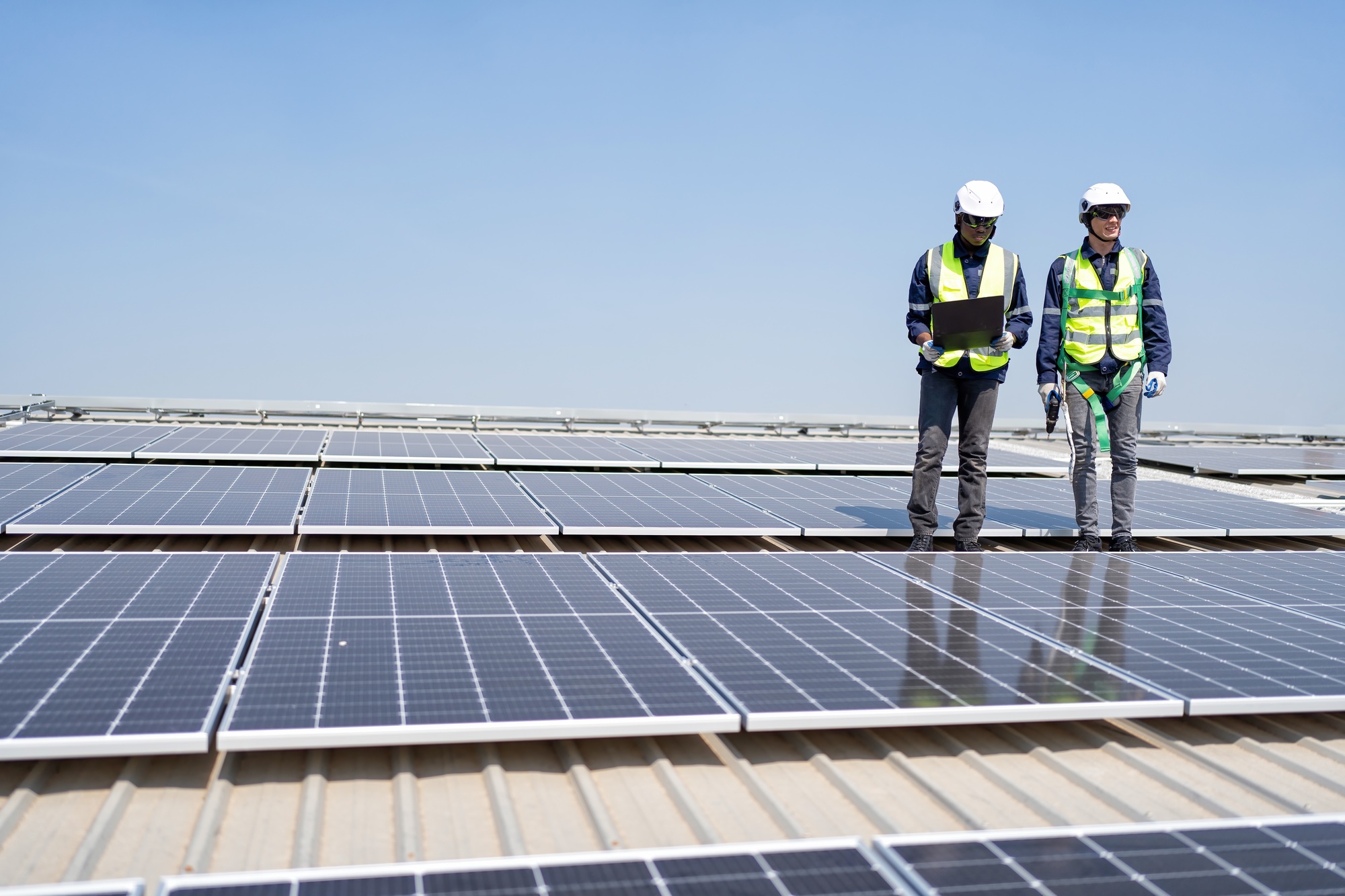 engineer-on-rooftop-stand-next-to-solar-panels-discussion-with-team-check-laptop-for-installation.jpg